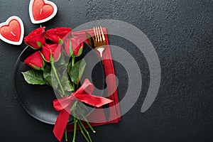 Valentines day romantic table setting. Empty closeup of red roses, wine, candles, dinner black plate, knife, fork and decorative