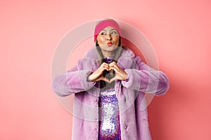 Valentines day and shopping concept. Cute and stylish asian senior woman pucker lips for kiss, showing heart sign, I