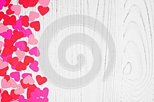 Valentines Day side border of heart confetti over a white wood background with copy space
