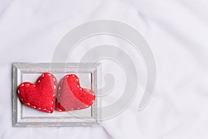 Valentines Day and symbol of love. Two red hearts in picture frame on white fabric background