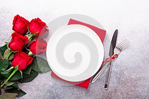 Valentines day table place setting with bouquet of red roses, red hearts on stone background. Top view. Valentine`s card