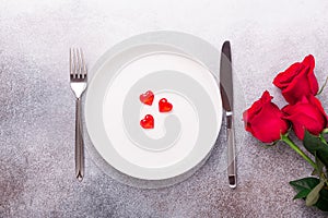 Valentines day table place setting with bouquet of roses, red hearts and silverware on stone background. Top view. Valentine`s