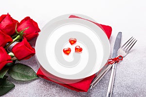 Valentines day table place setting with bouquet of roses, red hearts and silverware on stone background. Valentine`s card