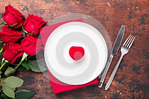 Valentines day table setting empty plate, red roses and velvet ring box on wooden background. Top view. Valentine`s greeting card