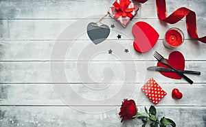 Valentines day table setting with fork, knife, red hearts, ribbon and roses.