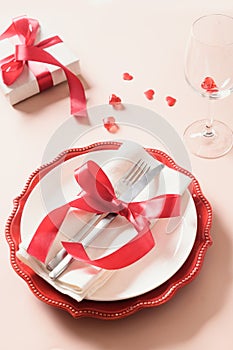 Valentines day table setting with gift, a bottle of red wine, roses, hearts.