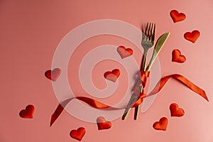 Valentines day table setting on a pink background. Golden cutlery and red hearts, romantic dinner concept