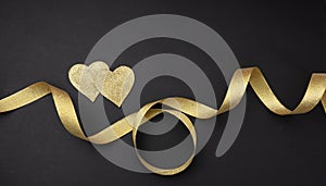 Valentines day. Top view of two golden hearts with satin ribbon against black background