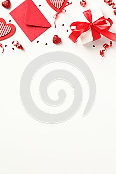 Valentines Day vertical background. Flat lay gift box with red ribbon bow, red envelope, hearts decorations, party streamers,