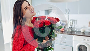 Valentines day. Young woman found bouquet of red roses on kitchen. Happy girl holding flowers