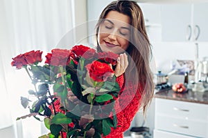 Valentines day. Young woman found bouquet of red roses on kitchen. Happy girl holding and smelling flowers