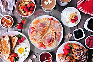 Valentines or Mothers Day breakfast table scene on a dark wood background with heart shaped pancakes, eggs and love themed food