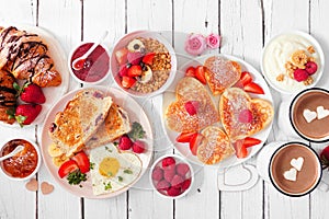 Valentines or Mothers Day breakfast table scene on a white wood background with heart shaped pancakes, eggs and love themed food