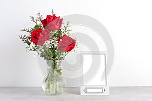 Valentineâ€™s day concept, Red roses flower bouquet in glass vase and blank grey vintage frame on table background with copy space