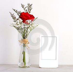 Valentineâ€™s day concept, Red roses flower bouquet in glass vase and blank grey vintage wooden frame on table background with