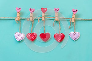 Valentineâ€™s Day. Sewed pillow hearts row border on red, pink and white clothespins at rustic blue pastel wall.