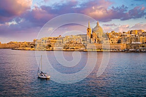 Valletta, Malta - St.Paul`s Cathedral in golden hour at Malta`s capital city Valletta with sailboat and beautiful colorful sky