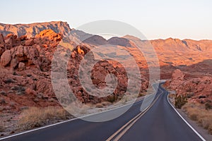 Valley of Fire - Panoramic sunrise view of endless empty road leading to red Aztec Sandstone Rock formations in Mojave desert