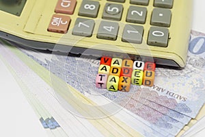 Value added tax texts on colorful alphabet beads and calculator over riyals banknotes