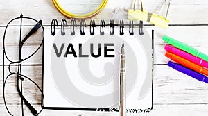 VALUE written in a notebook on white background with office tools