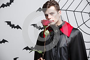 Vampire Halloween Concept - Portrait of handsome caucasian Vampire holding red beautiful rose.