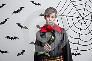Vampire Halloween Concept - Portrait of handsome caucasian Vampire holding red beautiful rose.