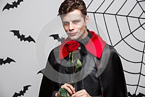 Vampire Halloween Concept - Portrait of handsome caucasian Vampire holding red beautiful rose.