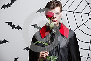 Vampire Halloween Concept - Portrait of handsome caucasian Vampire holding red beautiful rose.