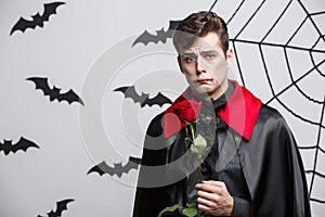 Vampire Halloween Concept - Portrait of handsome caucasian Vampire holding red beautiful rose.