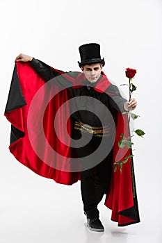 Vampire Halloween Concept - Portrait of handsome caucasian Vampire holding red beautiful rose on white studio background