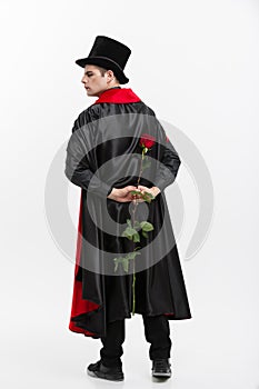 Vampire Halloween Concept - Portrait of handsome caucasian Vampire holding red beautiful rose on white studio background