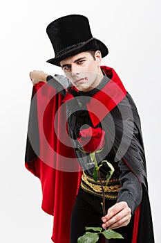 Vampire Halloween Concept - Portrait of handsome caucasian Vampire holding red beautiful rose on white studio background