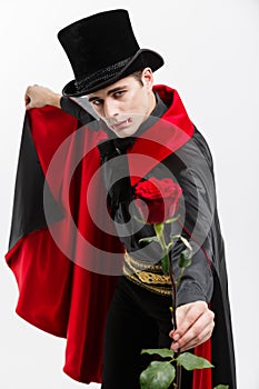 Vampire Halloween Concept - Portrait of handsome caucasian Vampire holding red beautiful rose on white studio background