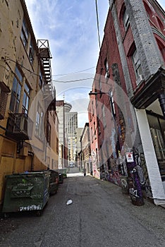 An narrow alleyway between colored old brick buildings and garbage containers at evening at the Vancouver downtown