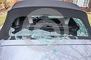 Vandalized soft top convertible sports car with back window smashed out and glass laying everywhere - close up photo
