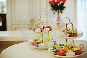 Vanilla bean mini cupcakes decorated with cyan and pink candy beads on a clear tiered tray on a dessert table.Sweet