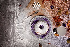 A vanilla cake with flowers on a plate. A New Year composition on a gray background. The inscription 2018 on a desk.