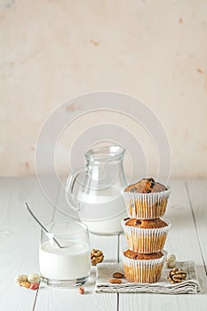 Vanilla caramel muffins in paper cups and glass of milk on white wooden background