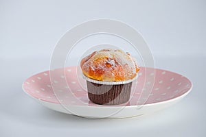 Vanilla cupcake in brown paper liners placed on a pink dish. side view