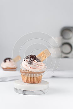 Vanilla cupcake with pink frosting, chocolate glaze and a cookie on a marble coaster