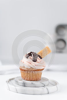 Vanilla cupcake with pink frosting, chocolate glaze and a cookie on a marble coaster