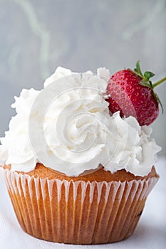 Vanilla cupcake with white frosting whip cream and a strawberry topper on a white background.