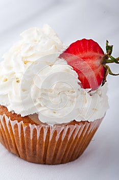 Vanilla cupcake with white frosting whip cream and a strawberry topper on a white background.