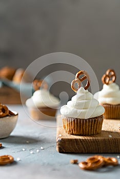 Vanilla cupcakes decorated with white frosting and brezel on dark table. Side view, close up, copy space. Cookbook recipe, menu,