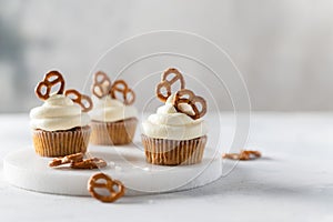 Vanilla cupcakes decorated with white frosting and brezel on white table. Side view, close up, copy space. Cookbook recipe, menu,