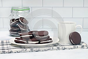 Vanilla filled chocolate sandwich cookies, stacked on a plate with some in a cookie jar