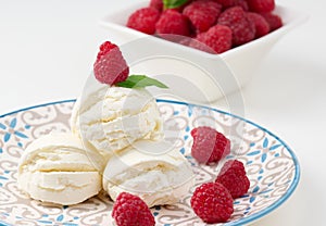 Vanilla ice cream balls with red raspberries in a round plate
