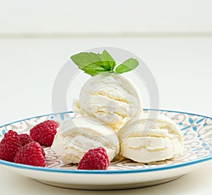 Vanilla ice cream balls with red raspberries in a round plate