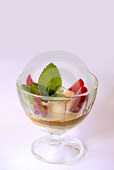 Vanilla ice cream with strawberries and chocolate sauce and mint leaves in a glass bowl over pastel pink background.