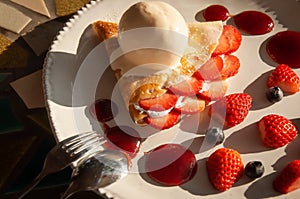 Vanilla ice cream on strawberry pie and blueberry on white plate